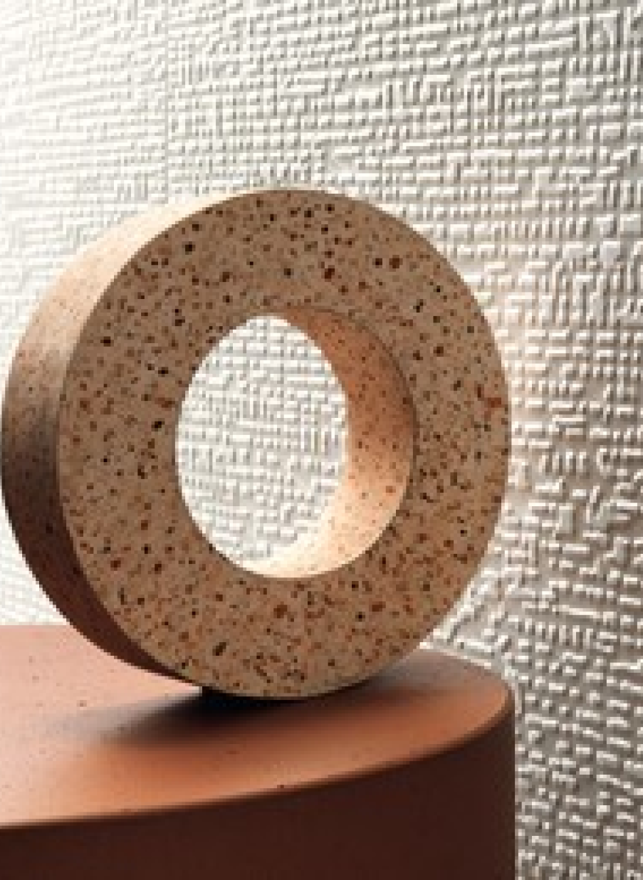 Superficie porcelánica texturada en tono terracota con pieza decorativa circular.